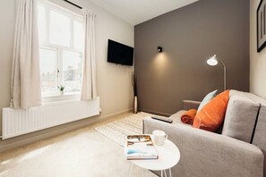 A modern living room with a sofa, a coffee table, a TV, and a window with curtains.