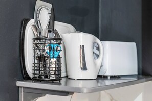 Eine Küchenarbeitsfläche mit Kaffeemaschine, Wasserkocher und Besteckhalter.