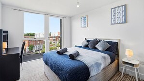 Una camera da letto moderna con un letto grande, una scrivania e un balcone che si affaccia sulla città.