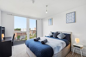A modern bedroom with a large bed, a desk, and a balcony with a city view. - #191 Mason Way Executive Stay - Sleeps 6 (West Midlands)