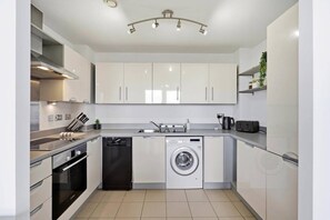 A modern kitchen with white cabinets, a dishwasher, a washing machine, and a built-in oven. - #191 Mason Way Executive Stay - Sleeps 6 (West Midlands)
