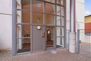 A building entrance with a glass door, a metal gate, and a brick wall. - #191 Mason Way Executive Stay - Sleeps 6 (West Midlands)
