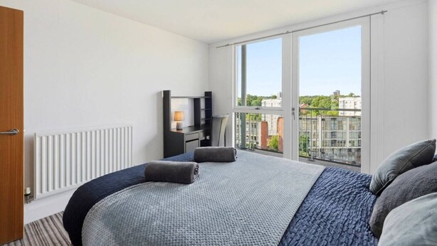 Una camera d'hotel moderna con un letto grande, una scrivania con una lampada e vista sulla città da una finestra ampia.