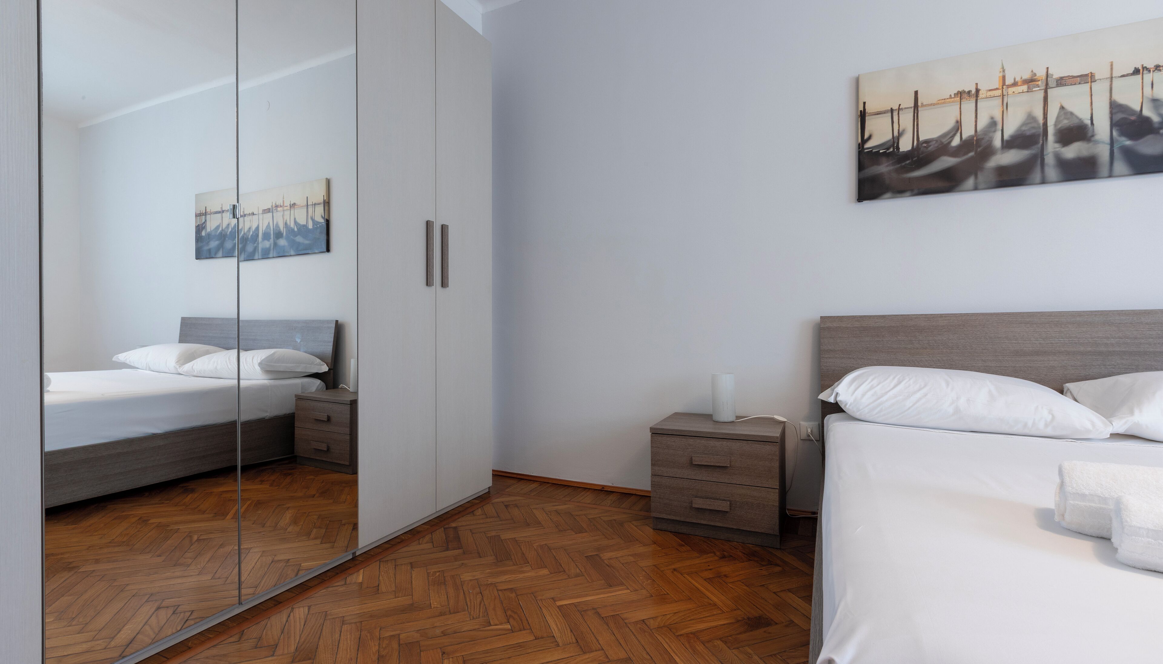 A modern bedroom with a bed, bedside tables, a nightstand, a mirror, and a painting on the wall.