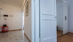 A hallway with a tiled floor, a door, a framed picture on the wall, and a red table with a black object on it. - Italianway Easy - De Cristoforis 12 A (Milan)