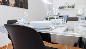 Et moderne spiseområde med et glasbord, hvide tallerkner og klare glas.