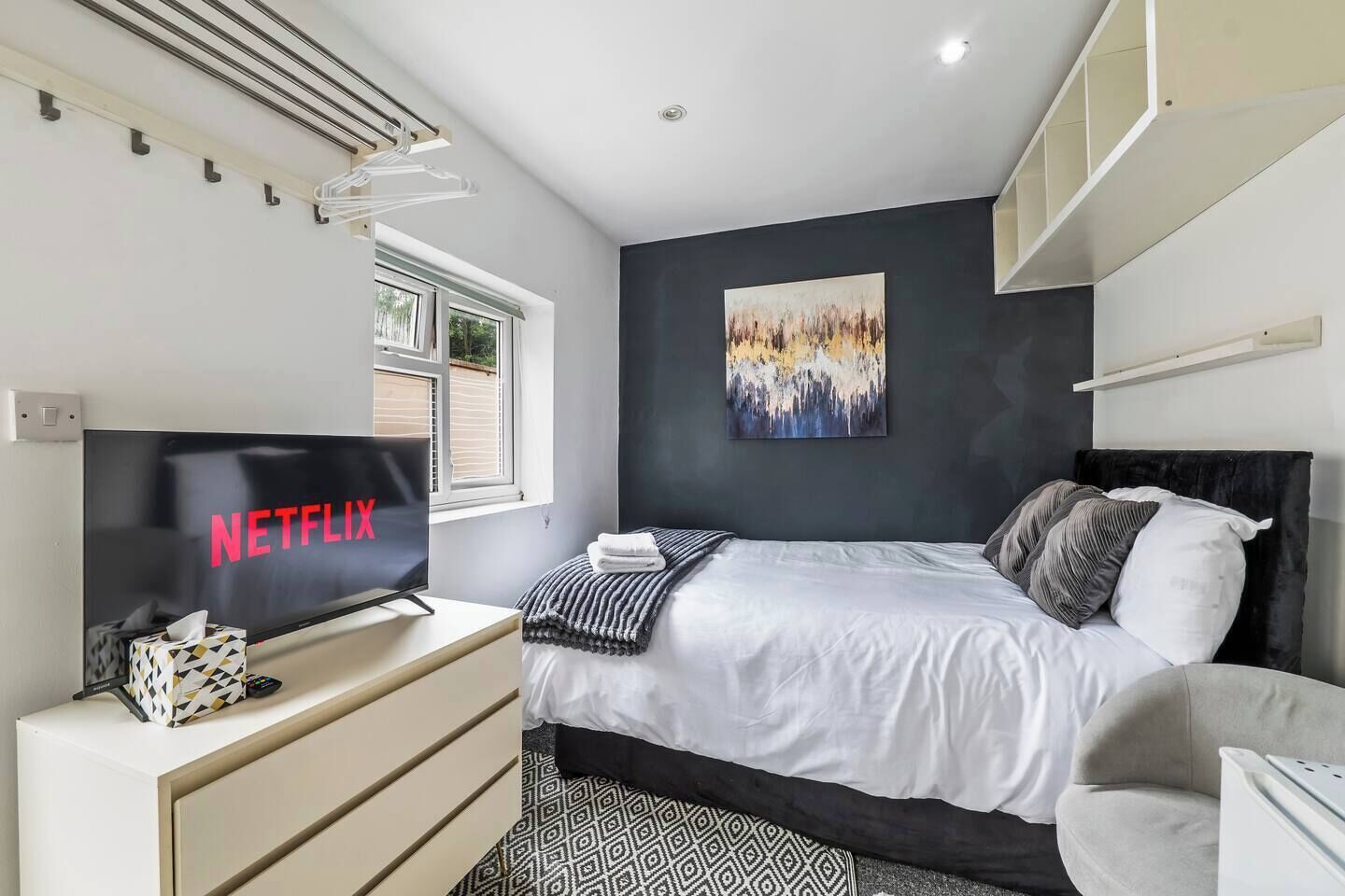 A modern bedroom with a bed, a TV, a painting, and a window.
