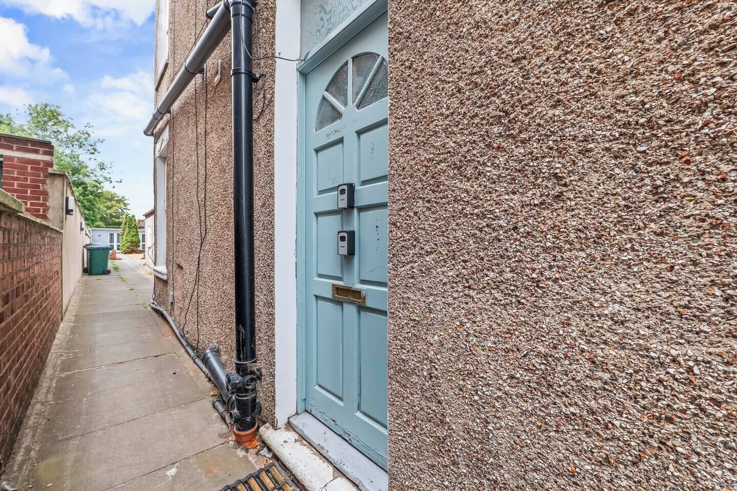 A narrow alleyway with a blue door, a brick wall, and a concrete path.