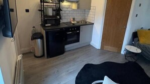 Uma cozinha compacta com eletrodomésticos modernos, uma área de refeições com uma cadeira e um pequeno espaço de estar com um almofada.