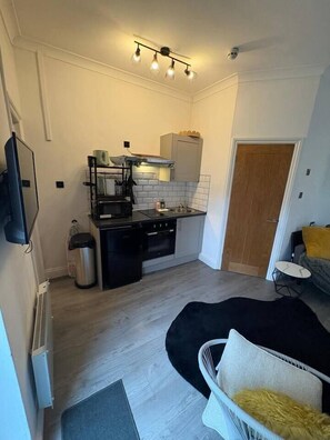 A compact kitchen with modern appliances, a dining area with a chair, and a small seating area with a cushion. - #194 Smart Coventry Studio | Ideal for 2 (West Midlands)