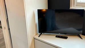 Uma televisão sobre um móvel branco, com o controle remoto ao lado.