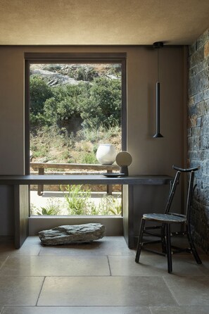 A room with a large window, a stone wall, a bench, a chair, and a hanging light fixture. - The Tierras - Tērra | 2 Bedroom Maisonette Private Pool Villa (Heraklion)