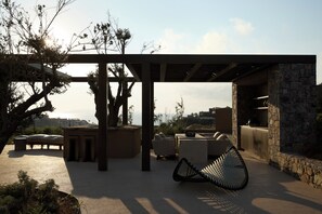 Ein Sitzbereich im Freien mit einer Pergola, Steinmauern und Blick aufs Meer.