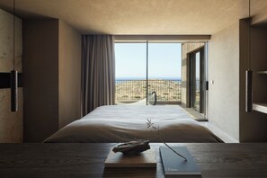 Ein Schlafzimmer mit einem großen Bett, Meerblick vom Balkon und einem Holztisch mit einem Buch und einem Zweig.