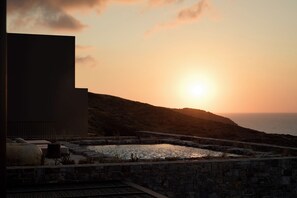Ein Sonnenuntergangsblick von einer Terrasse mit Pool, mit Blick auf das Meer und eine hügelige Landschaft.