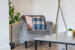 Una armchair gris amb un coixí de vellesa i una petita planta en test amb flors grogues.