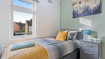 A bedroom with a bed, bedside table, lamp, and a painting on the wall.
