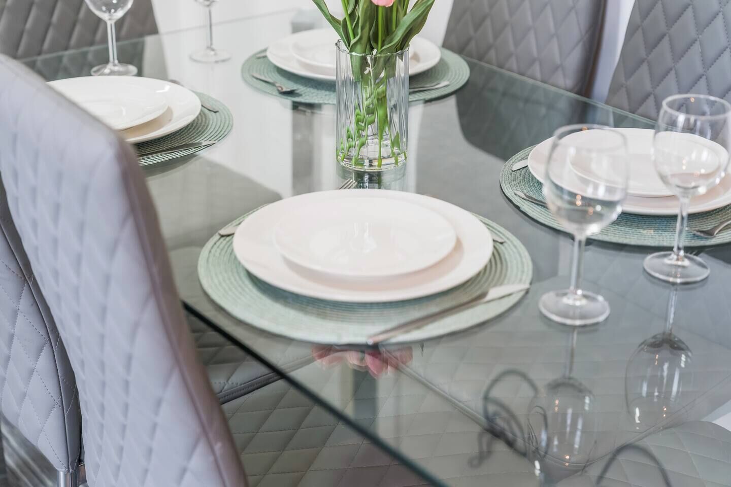 A dining table set with plates, glasses, and a vase with flowers.
