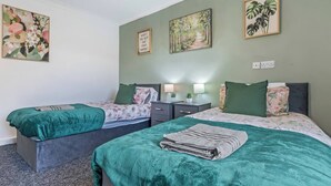 Ein Zimmer mit zwei Betten, jeweils mit einer grünen Bettdecke, einem Nachttisch mit einer Lampe und einer Wand mit drei gerahmten Bildern.