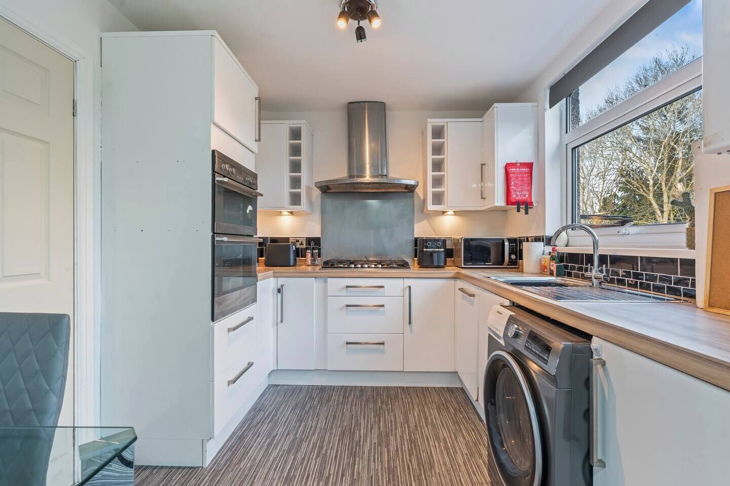 A modern kitchen with white cabinets, stainless steel appliances, and a large window providing natural light.