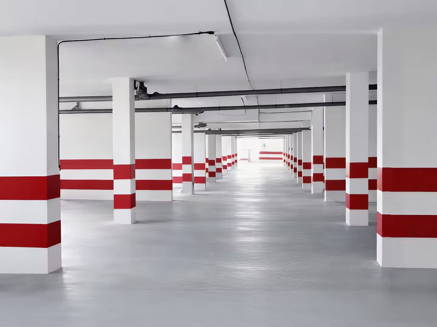 Un long couloir vide, orné de piliers blancs et rouges, qui mène à une sortie lumineuse.