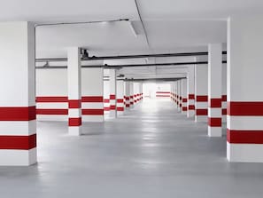 A long, empty corridor with white and red pillars, leading to a bright exit.