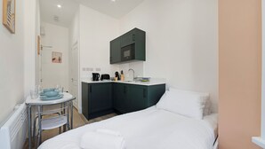 Ett kompakt hotellrum med en säng, ett litet pentry, ett runt bord med stolar och ett enda konstverk på väggen.