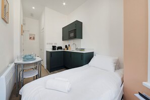 A compact hotel room with a bed, a small kitchenette, a round table with chairs, and a single artwork on the wall. - Charmstay Westbourne PArk (London)