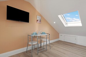 A room with a flat-screen TV mounted on the wall, a small table with chairs, and a skylight. - Charmstay Westbourne PArk (London)