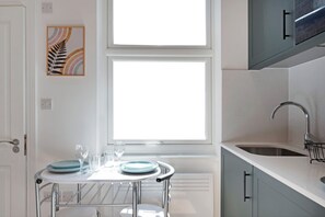 Eine Küche mit Fenster, Tisch mit Tellern und Gläsern sowie einem Spülbecken.