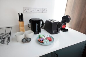 A kitchen counter with a coffee maker, toaster, mug, and a plate with food items. - Charmstay Westbourne PArk (London)