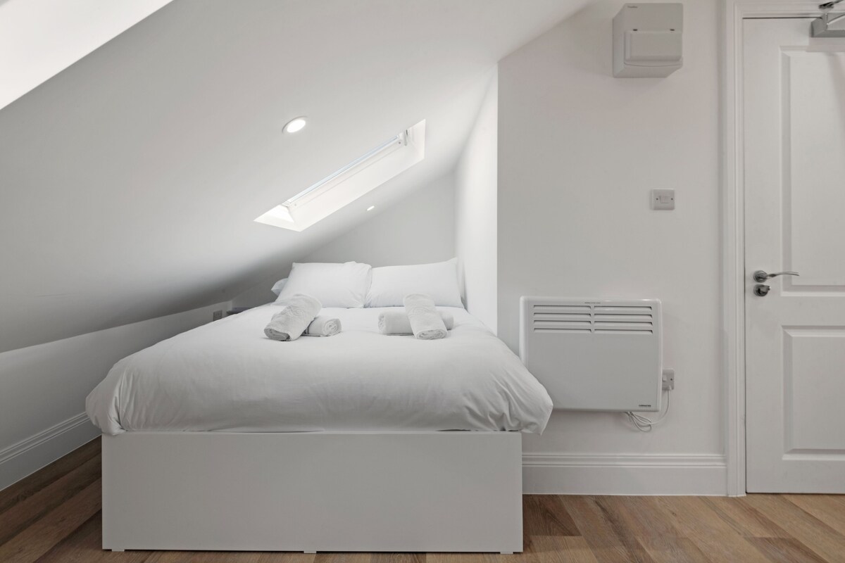 A modern, white-themed bedroom with a bed, a radiator, and a door.