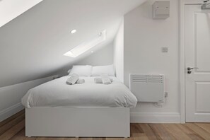 Ein modernes, weiß eingerichtetes Schlafzimmer mit Bett, Heizkörper und Tür.