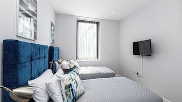 A modern bedroom with a large bed, a smaller bed, a TV, and a window with blinds.