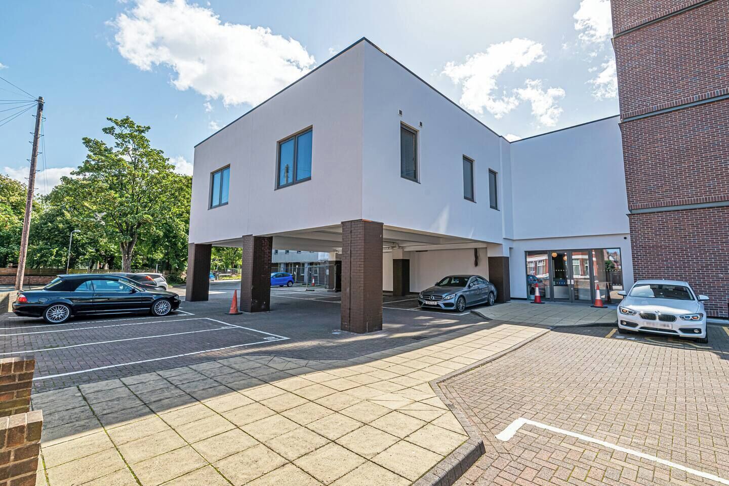 Een modern gebouw met een plat dak, grote ramen en een parkeerplaats met auto's.