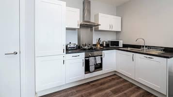 Een moderne keuken met witte kasten, een roestvrijstalen afzuigkap, een magnetron en een spoelbak met een afdruimte.