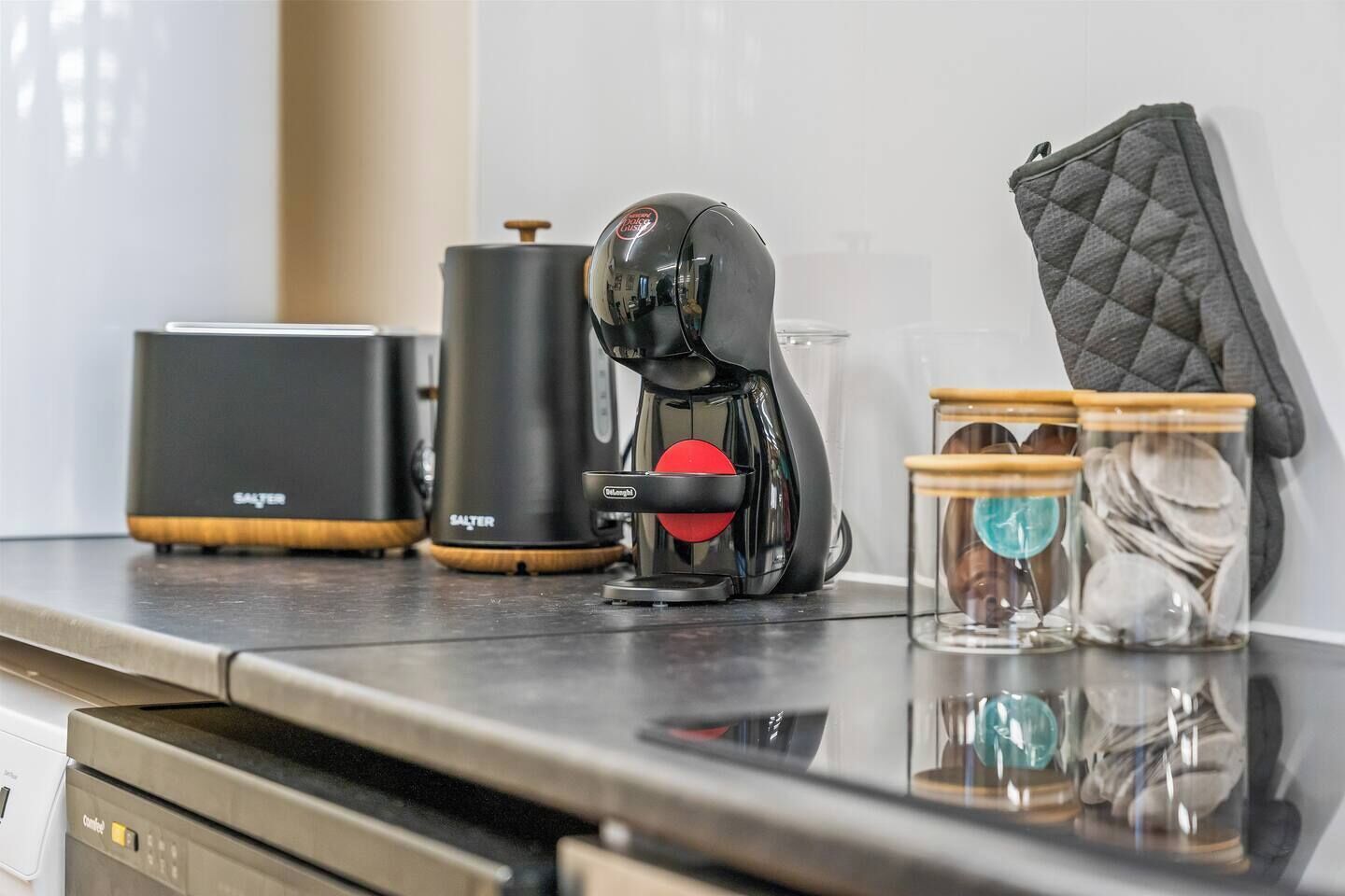 A kitchen counter with a coffee maker, a kettle, and two glass jars with lids.