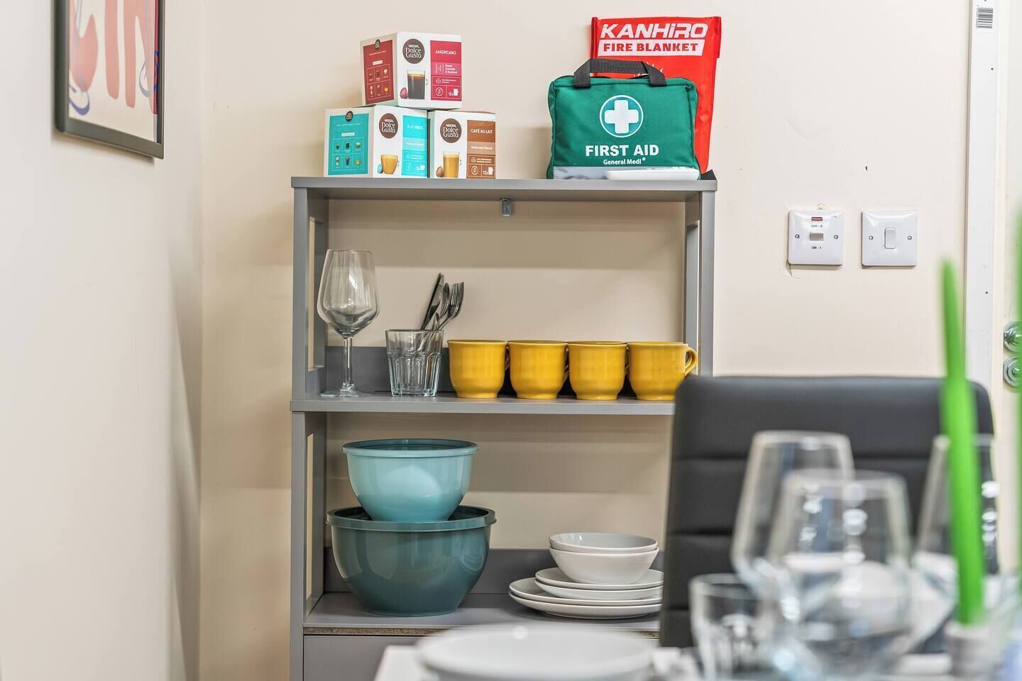 A shelf with various items including a first aid kit, a fire blanket, and boxes of coffee.