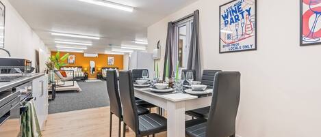A modern dining area with a white table set for four, black chairs, and a kitchen area with a stove and sink.