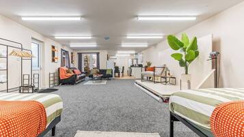 A modern, well-lit room with a sofa, two beds, a desk, and a plant.