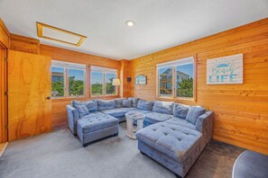 Ein Zimmer mit einem großen, L-förmigen Ecksofa, einem kleinen runden Tisch und einem Fenster mit Blick auf ein Gebäude.