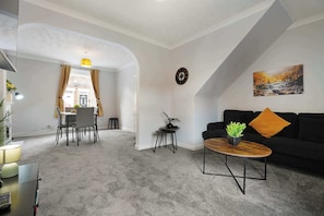 Ein modernes Wohnzimmer mit einer schwarzen Couch, einem runden Couchtisch und einem Essbereich mit Tisch und Stühlen.