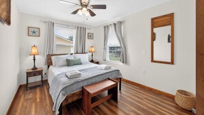 Una camera da letto con un letto, lampade sui comodini, una ventola a soffitto e un'ampia finestra con tende.