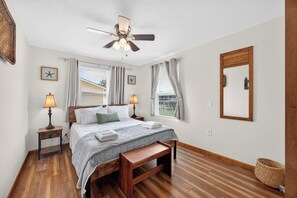 Ein Schlafzimmer mit einem Bett, Nachttischlampen, einem Deckenventilator und einem großen Fenster mit Vorhängen.