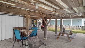 Un'area patio esterna coperta con un tavolo e sedie in legno, una sedia in vimini e un tavolo da picnic.