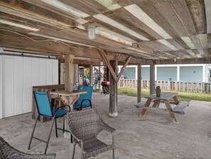 Ein überdachter Außenbereich mit Holztable und -stühlen, einem Korbstuhl und einem Picknicktisch.