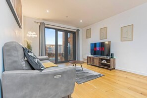 Ein modernes Wohnzimmer mit einem grauen Sofa, einem Flachbildfernseher und Holzboden.