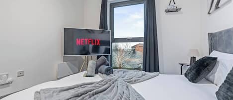 Habitación de hotel con una cama, un televisor mostrando 'NETFLIX', una ventana con cortinas y vistas a edificios.