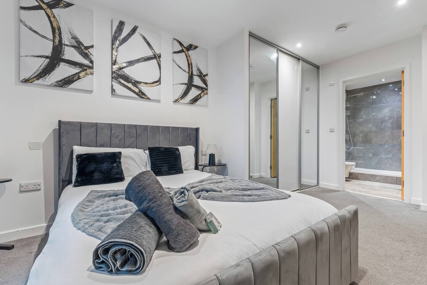 A modern bedroom with a large bed, a walk-in closet, and a bathroom with a glass shower.