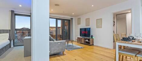 A modern living room with a sofa, a dining table set for two, and a television displaying 'NETFLIX'.